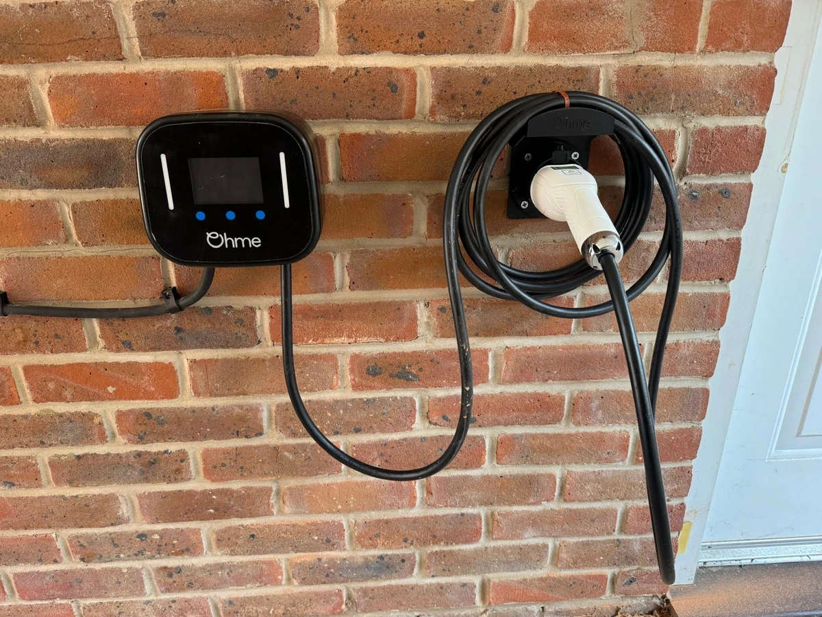 Ohme charge point and coiled tethered lead on brickwork