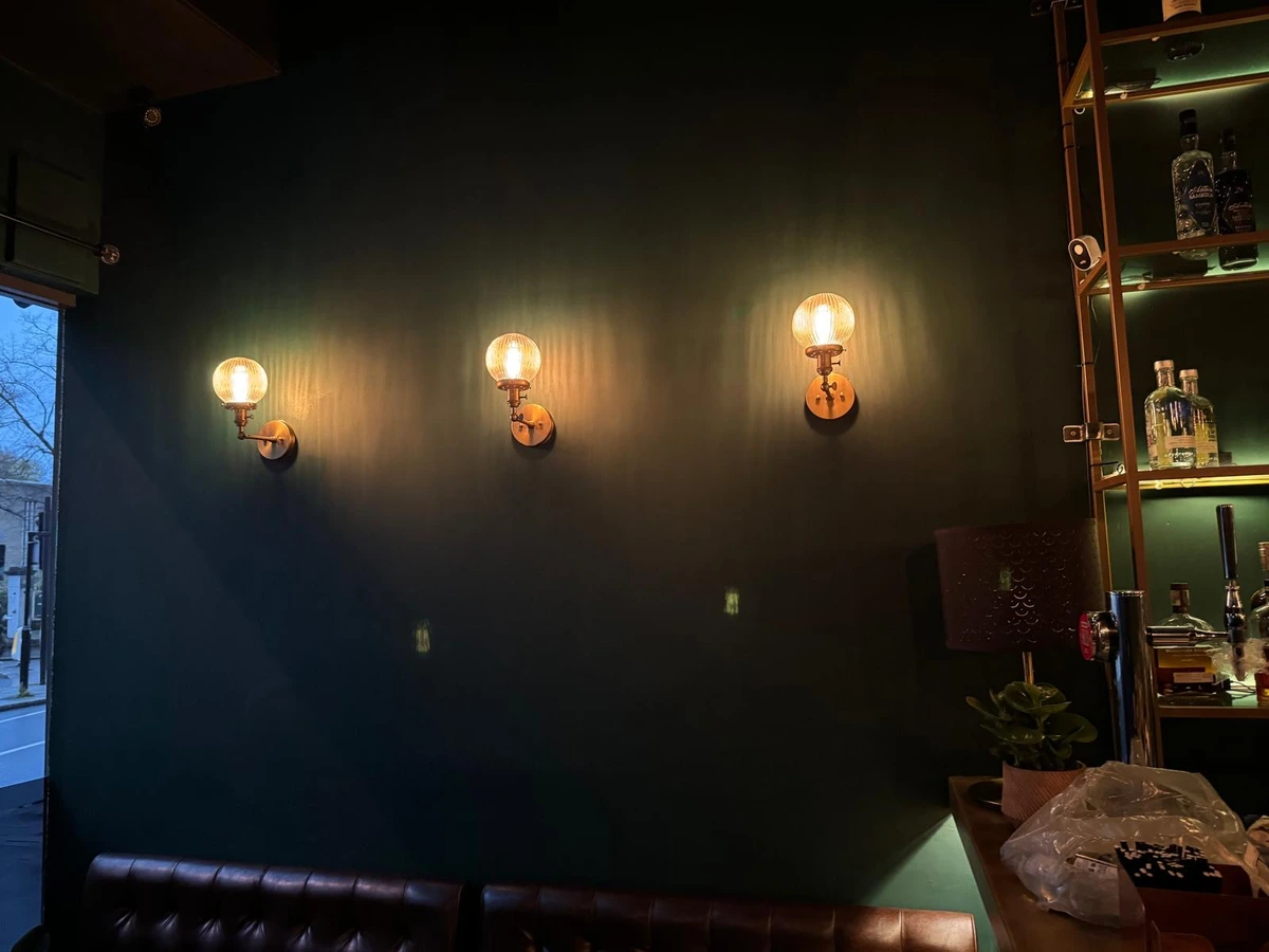 Three wall lights spaced along a dark painted bar wall